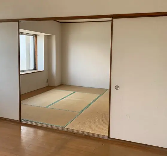 木目調のフローリングの部屋から、引き戸で仕切られた畳敷きの和室を見た室内風景。和室には窓があり、部屋は空室。
