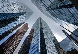 高層ビル群を見上げる仰角からの建築写真。ガラス張りの現代的なオフィスビルが青空に向かってそびえ立つ都市景観