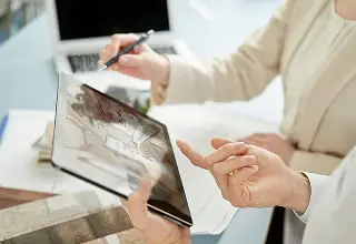 タブレット画面に表示された住宅のCGイメージを確認している様子。明るい木目調のフローリングとシンプルなインテリアの室内が表示されている